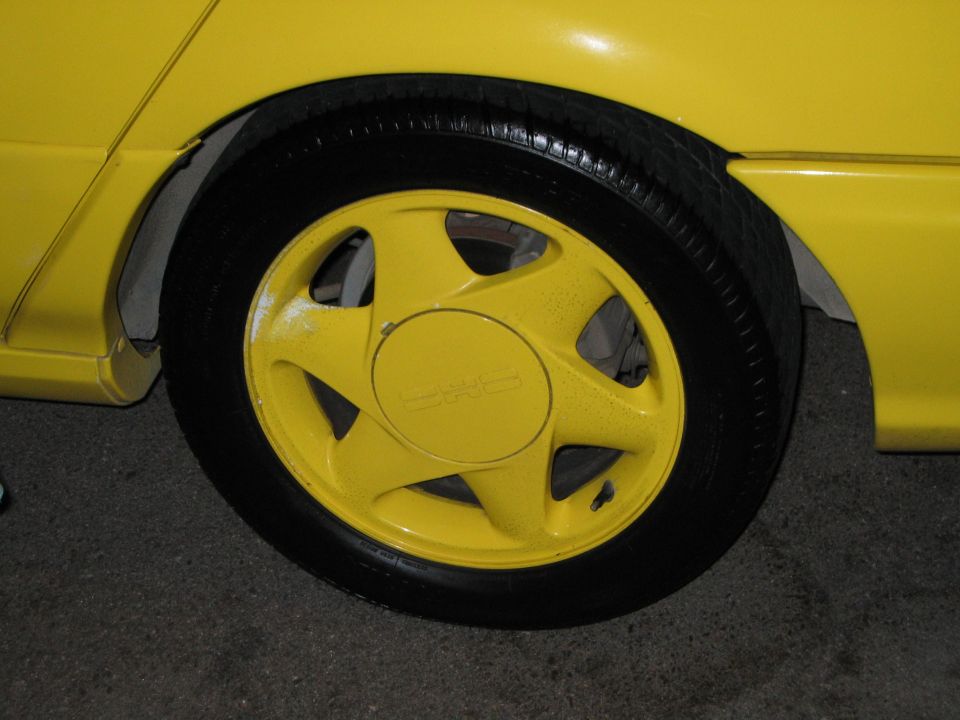 Yellow car wheel with a five-spoke design. The center cap has some text on it