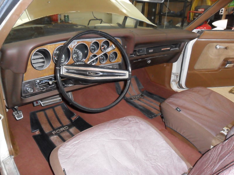 Brown and maroon vintage Ford interior with woodgrain dash, round gauges, and black steering wheel