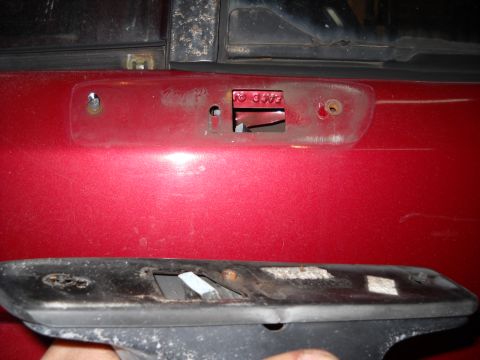 1993 Ford C-150 (Centurion Conversions) - Door handle assembly removed from a red vehicle door, revealing mounting points and internal mechanisms.