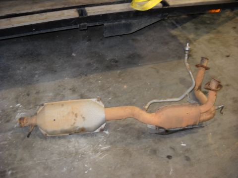 1993 Ford C-150 (Centurion Conversions) - A used exhaust system, including a catalytic converter and muffler, lies on a concrete floor.