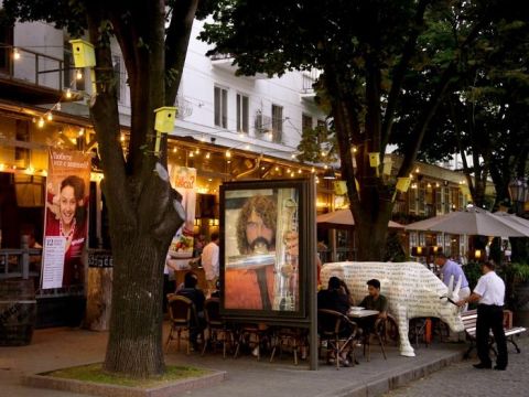 1990 Ford Bronco - An art installation of a cow covered in text is displayed near an outdoor cafe.