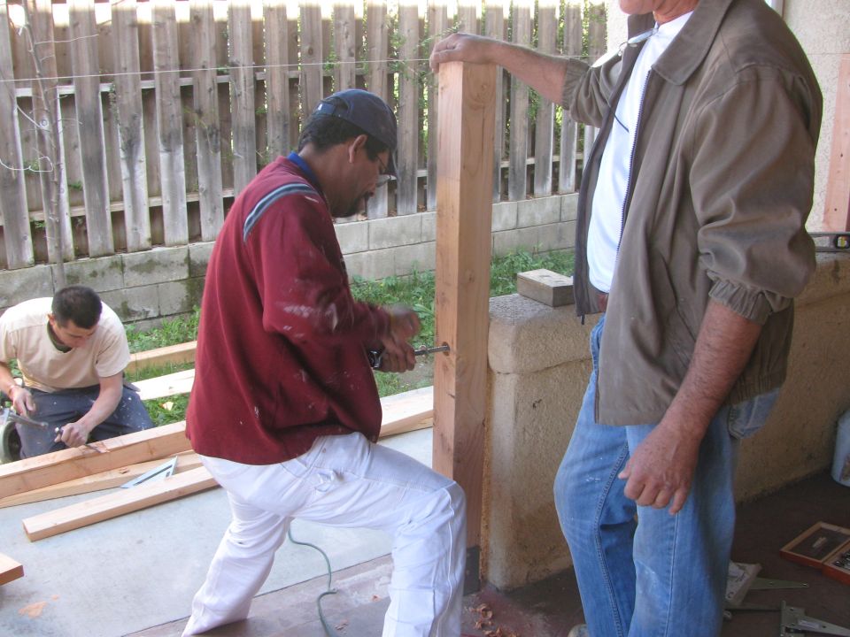 Three men working on wooden posts and lumber outdoors