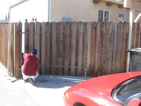 1968 Ford Mustang - A person is kneeling to repair a section of a weathered wooden fence.