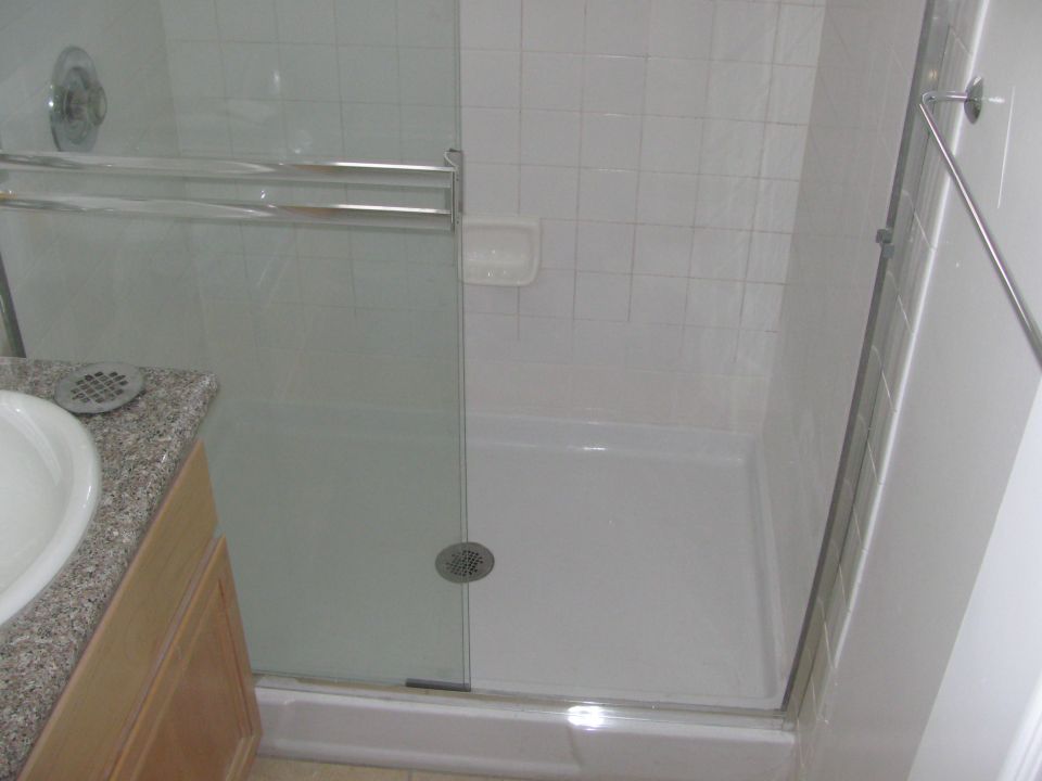 Bathroom shower stall with glass doors, white tiled walls, and a granite-topped vanity with a sink