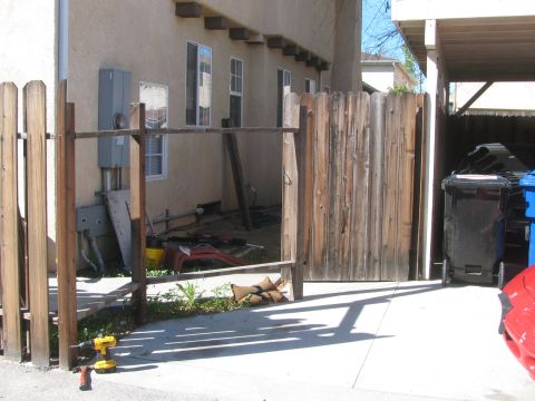 1968 Ford Mustang - A red car part is visible on a driveway, with a wooden fence and trash cans in the background.