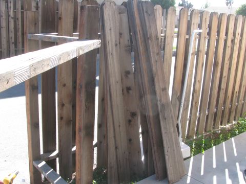 1968 Ford Mustang - Stacked lumber leans against a wooden fence on a sunny day.