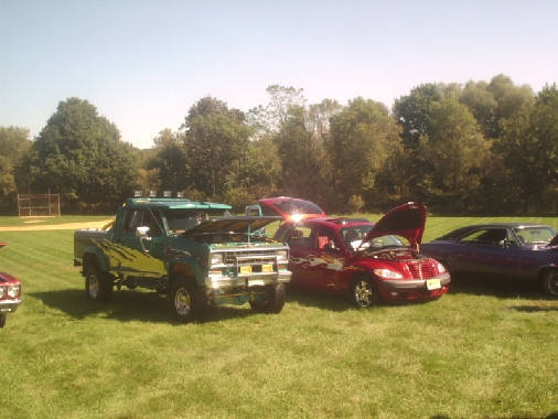 Green pickup truck with yellow graphics and lifted suspension, hood open, parked on grass