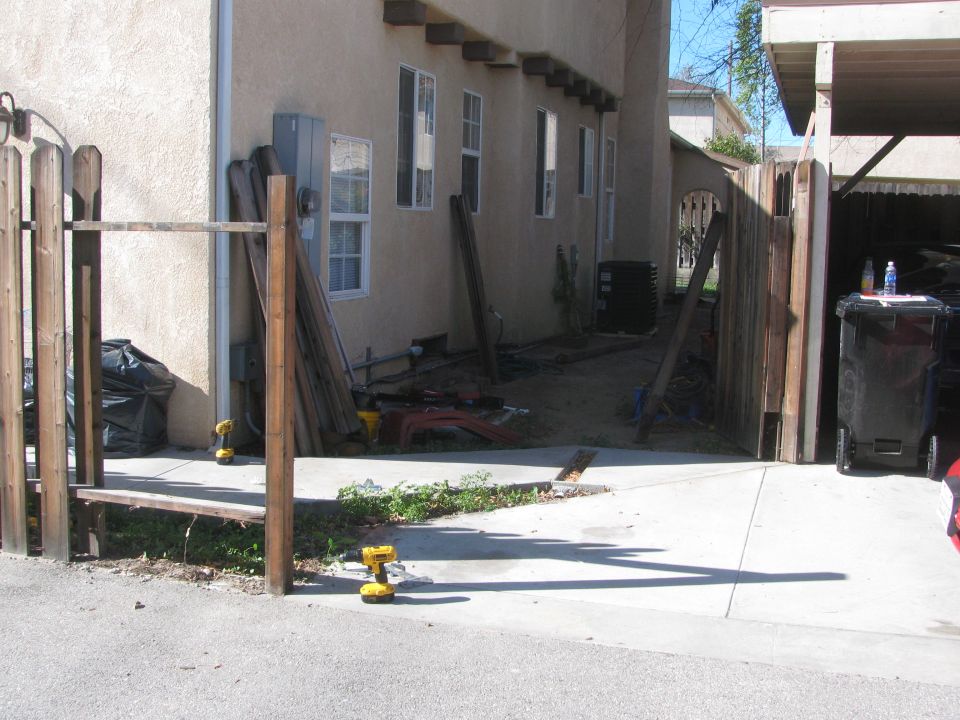 Construction scene with two yellow drills on concrete, wooden fence, and building materials