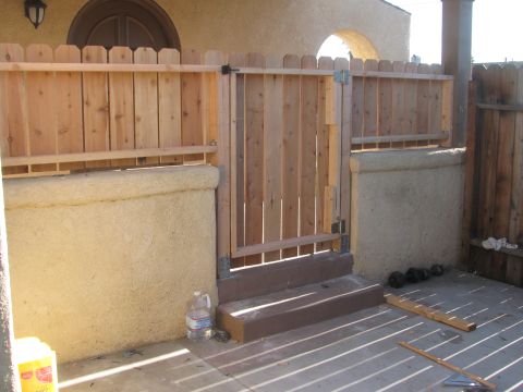 1968 Ford Mustang - A newly constructed wooden fence and gate with a stucco wall and concrete patio. Some weights are visible on the ground.