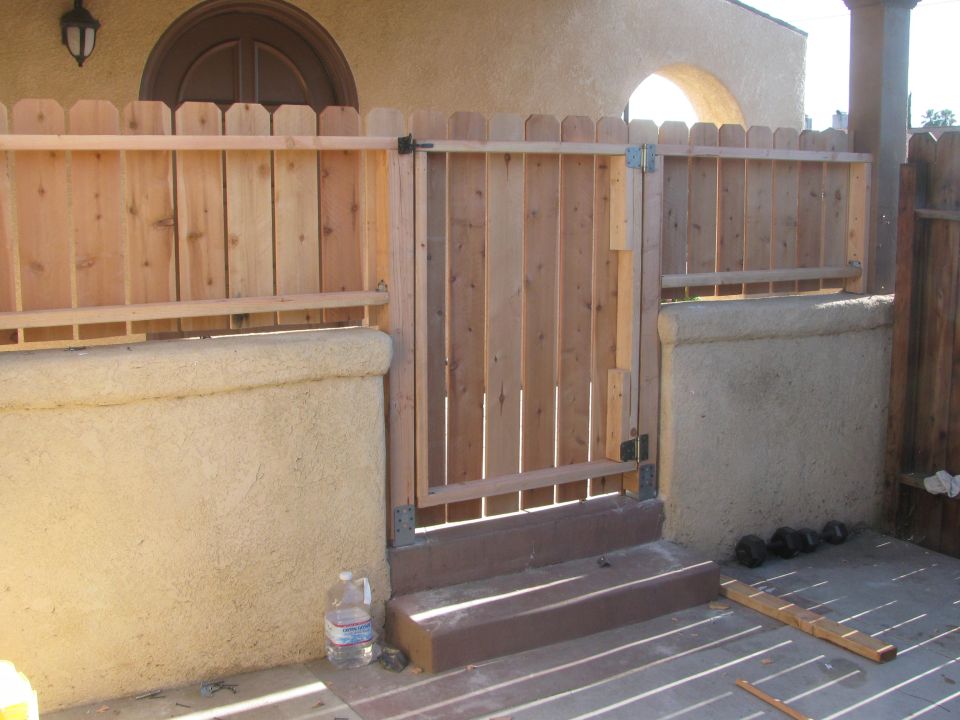 Wooden fence with a gate, stucco wall, and a water bottle on a patio