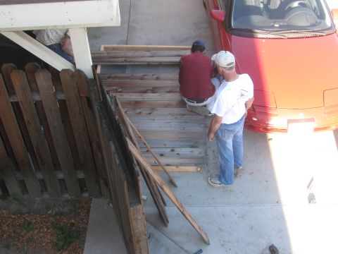 1968 Ford Mustang - A red car is parked next to a wooden fence and a set of stairs under construction.