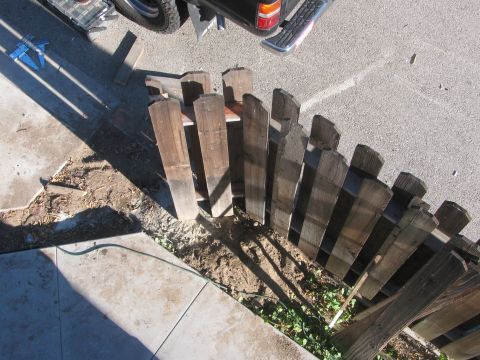 1968 Ford Mustang - Construction materials for a wooden fence are staged near a sidewalk and road.