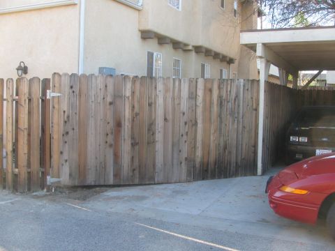 1968 Ford Mustang - A red car's front corner and a black car's rear are partially visible next to a wooden fence and carport.