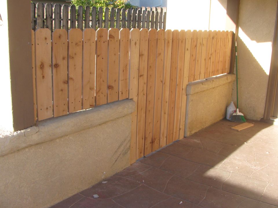 Wooden fence with a concrete base and a stamped concrete patio. A broom and cleaning supplies are visible