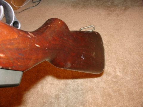 2003 Ford Crown Victoria - The worn wooden stock of a firearm is shown in detail, resting on a carpeted surface.