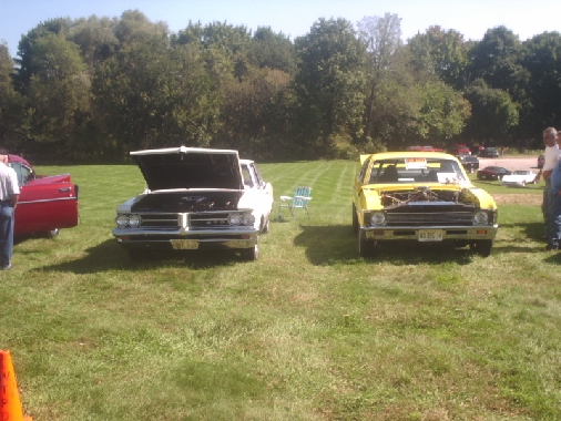 White car with hood up next to yellow car with hood up at outdoor car show