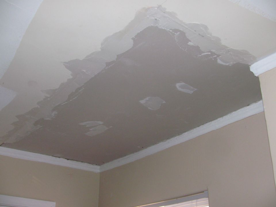 Damaged ceiling with peeling paint and drywall patches, showing unfinished repairs