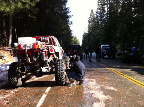 1989 Ford Bronco - Several off-road vehicles are stopped on a road in a wooded area, with one vehicle's rear tire being serviced.