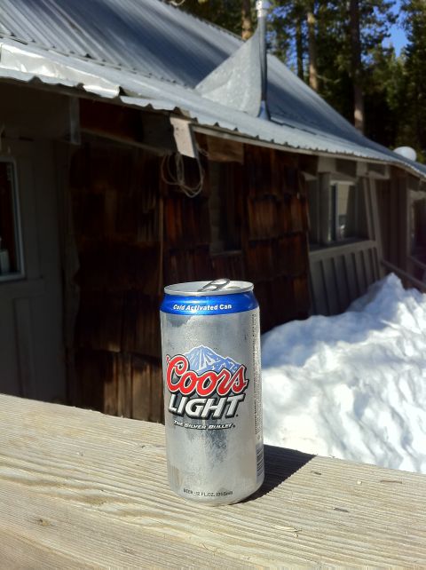 1989 Ford Bronco - Coors Light can sits on a wooden railing with a snow-covered landscape and cabin behind it.