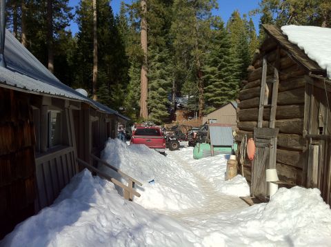 1989 Ford Bronco - A red pickup truck is partially buried in snow next to a log cabin in a wooded area.