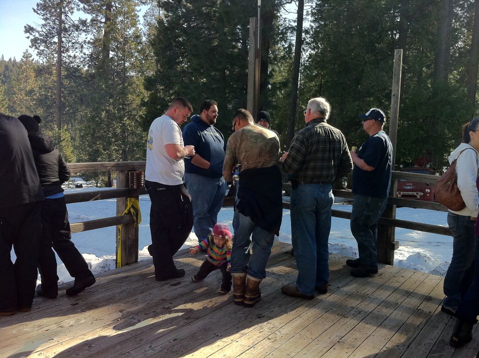 People gathered on a wooden deck with snow on the ground and trees in the background