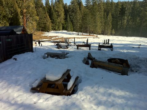 1989 Ford Bronco - A winter scene shows picnic tables and fire pits partially buried in snow, surrounded by a forest.