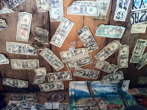 1989 Ford Bronco - Many dollar bills are covered in handwritten messages and dates, pinned to a rustic wooden surface.