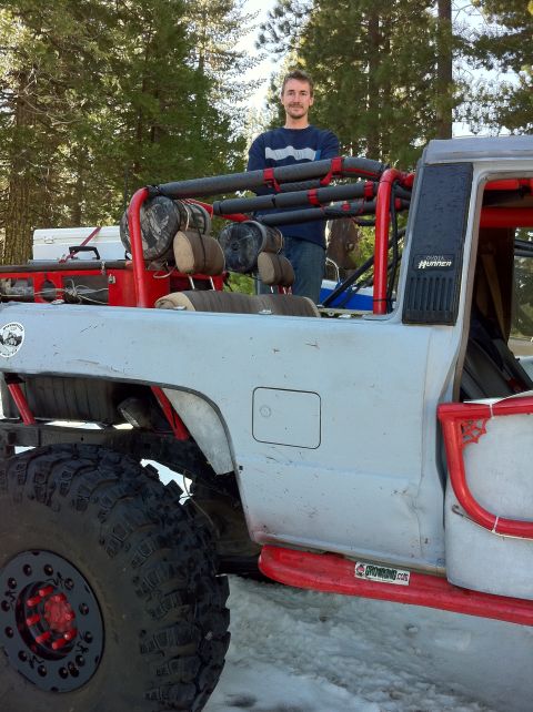 1989 Ford Bronco - Modified SUV with roll cage and large tires. A man stands behind the vehicle in a wooded area.