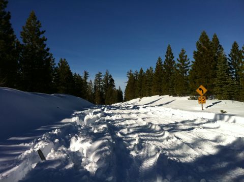 1989 Ford Bronco - A snow-covered mountain road with tire tracks suggests recent vehicle passage, despite the clear blue sky.