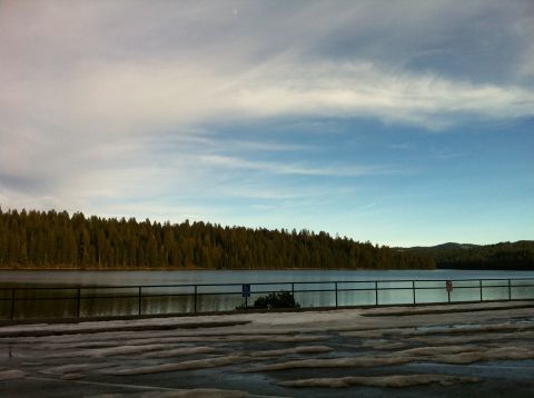 1989 Ford Bronco - A tranquil scene of a lake bordered by a forest, with a partially snow-covered parking lot in the foreground under a cloudy sky.