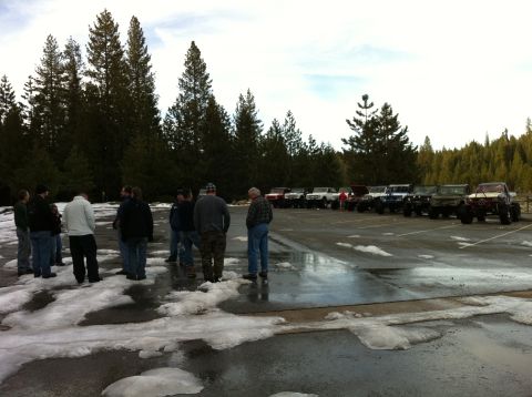 1989 Ford Bronco - A group of people stand in a snowy parking lot next to a line of off-road vehicles.