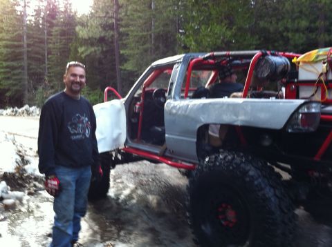 1989 Ford Bronco - A man poses next to a custom-built off-road pickup truck in a wooded area.