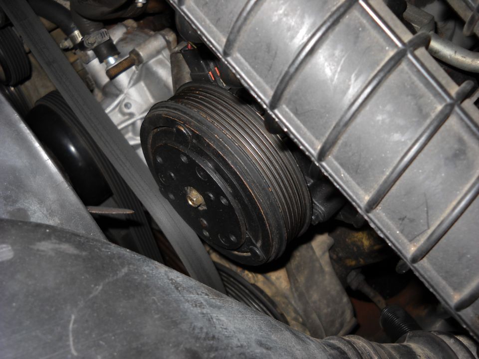Close-up of engine belt and pulley system, likely an AC compressor clutch