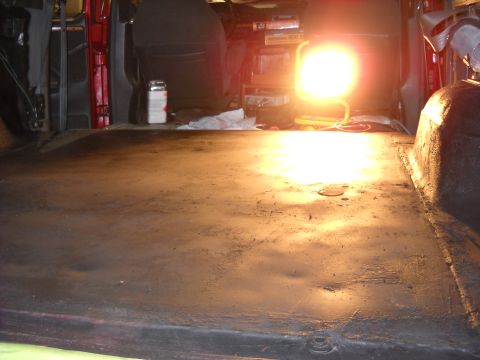1993 Ford C-150 (Centurion Conversions) - The dark floor of a vehicle's cargo area is lit by a bright work light, revealing some dents and wear.