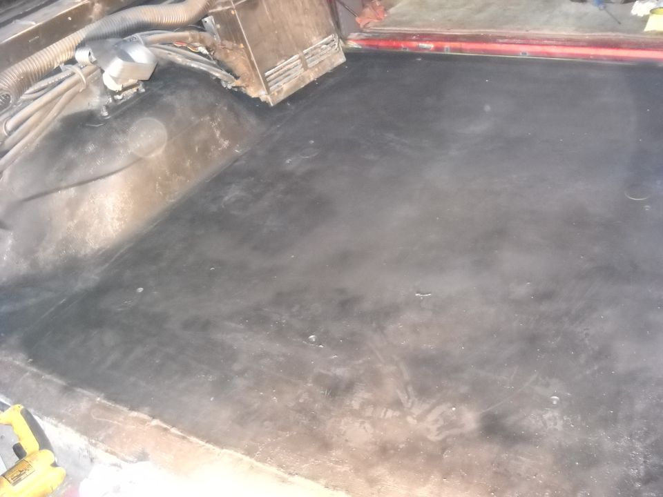 Interior floor of a vehicle, showing the black matting and some wiring and a metal box