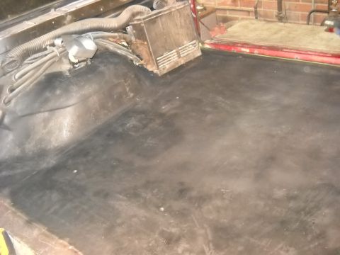 1993 Ford C-150 (Centurion Conversions) - The dark, worn floor of a vehicle's interior shows signs of wear and tear, with exposed wiring and a vent housing.
