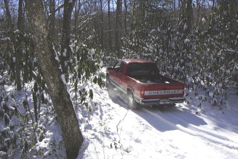 1995 Ford Bronco - A red Chevrolet pickup truck navigates a snow-covered path through a wooded area.