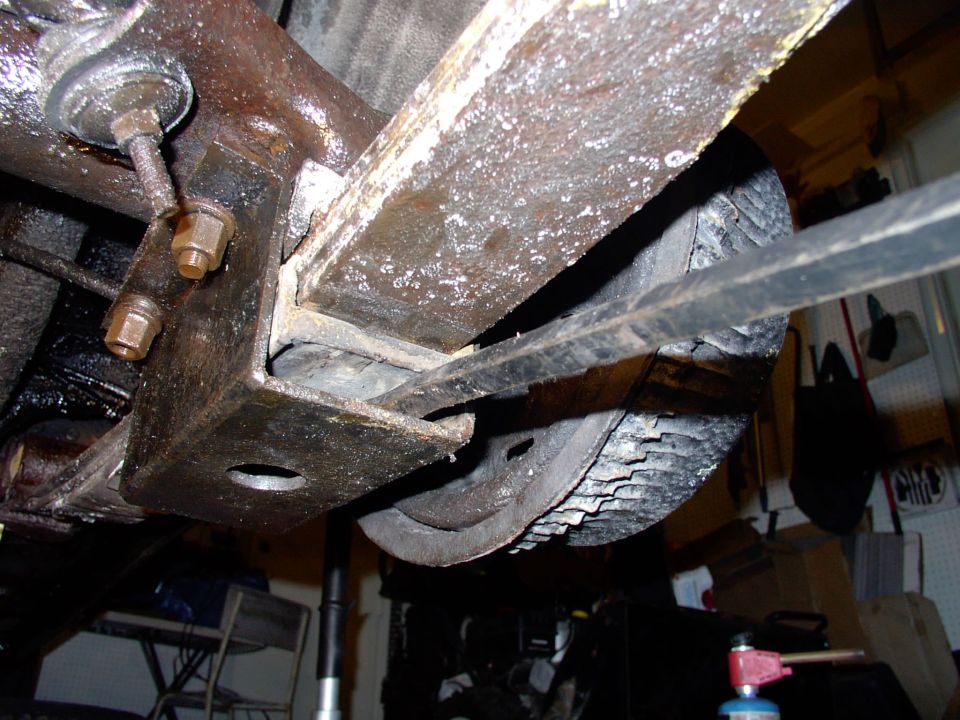 Underside view of rusty rear leaf spring, shackle mount and tire on a vehicle in a garage