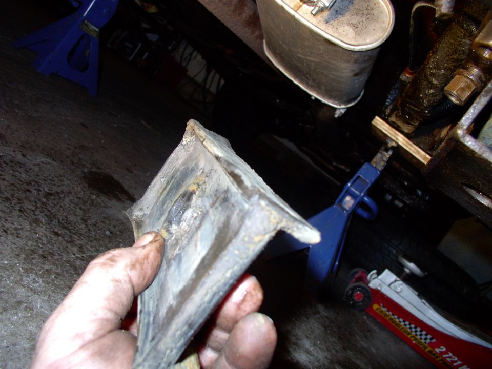 Dirty hand holding a removed rubber mount under a car supported by blue jack stands in a garage