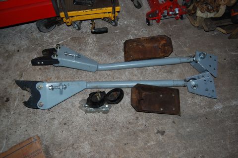 1994 Ford Bronco - Two suspension arms and associated parts are laid out on a concrete floor.