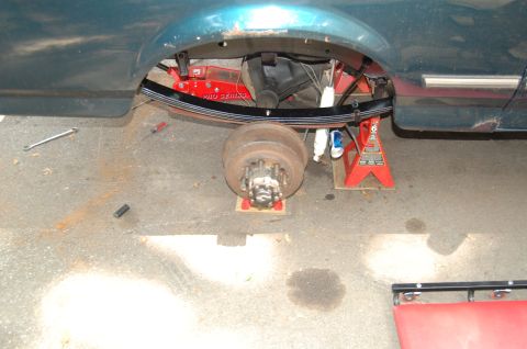 1994 Ford Bronco - The rear suspension of a teal SUV is disassembled, with the axle supported by jack stands.