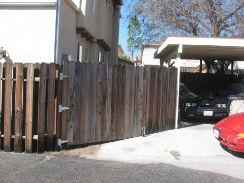 1968 Ford Mustang - A black coupe is parked under a carport, partially obscured by a wooden fence. A red car is also visible.