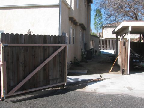 1968 Ford Mustang - A residential scene showing a driveway, a wooden gate, and a car parked in a carport.