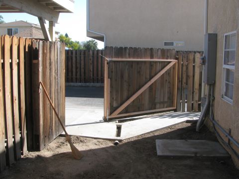 1968 Ford Mustang - A wooden gate stands open in a backyard fence, with a broom resting nearby.