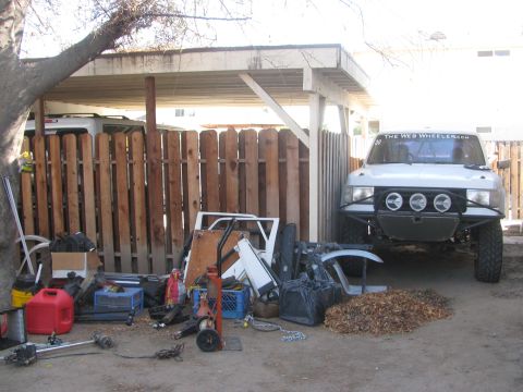 1968 Ford Mustang - A white off-road truck is parked under a carport, with various parts and debris scattered around.