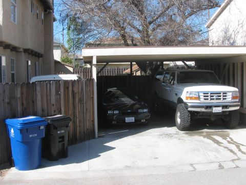 1968 Ford Mustang - Two vehicles are parked under a carport, with trash cans visible to the left.