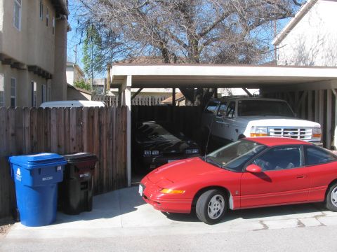 1968 Ford Mustang - Multiple vehicles parked in a driveway under a carport on a sunny day.