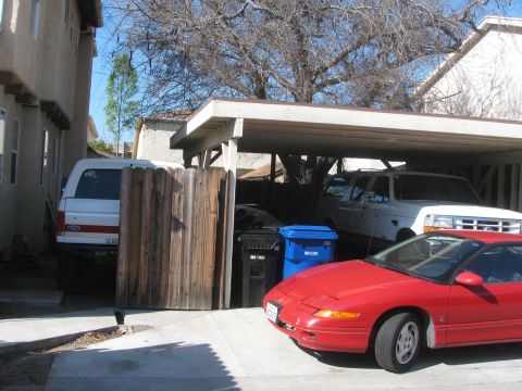 1968 Ford Mustang - A red sports car is parked in front of a carport, with two trucks visible behind it.