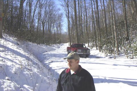 1995 Ford Bronco - A red pickup truck is parked on a snow-covered road in a wooded area.