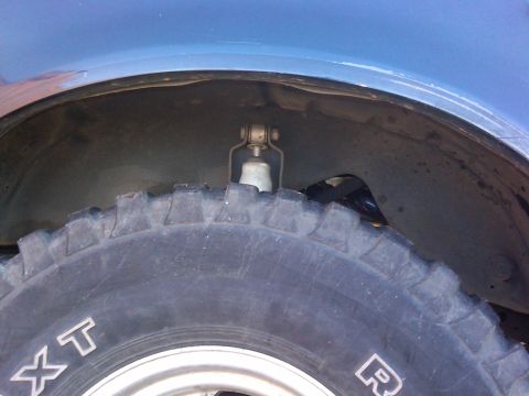 1988 Ford Bronco - A close-up view of a vehicle's tire and wheel well, showing the shock absorber and part of the suspension system.